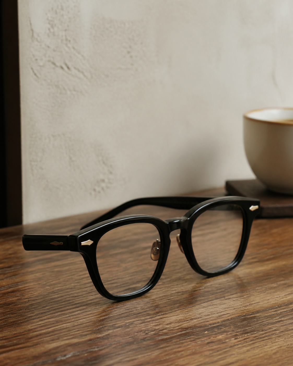 Dark acetate eyeglasses on walnut beside a coffee cup